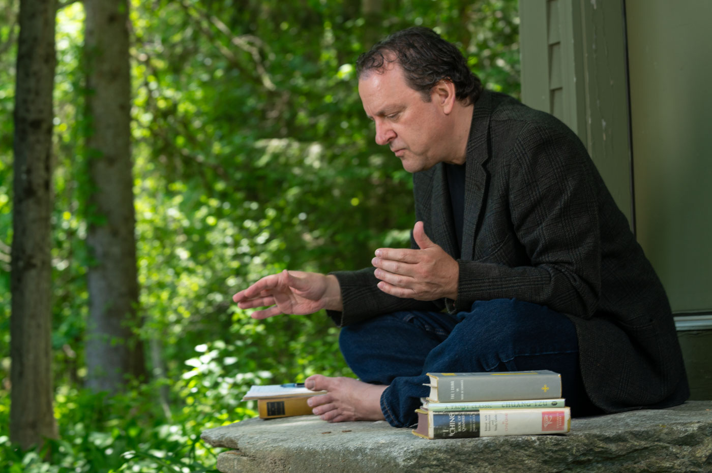 Adam Bauer seated cross-legged on stone in the woods, teaching, his vintage I Ching books beside him